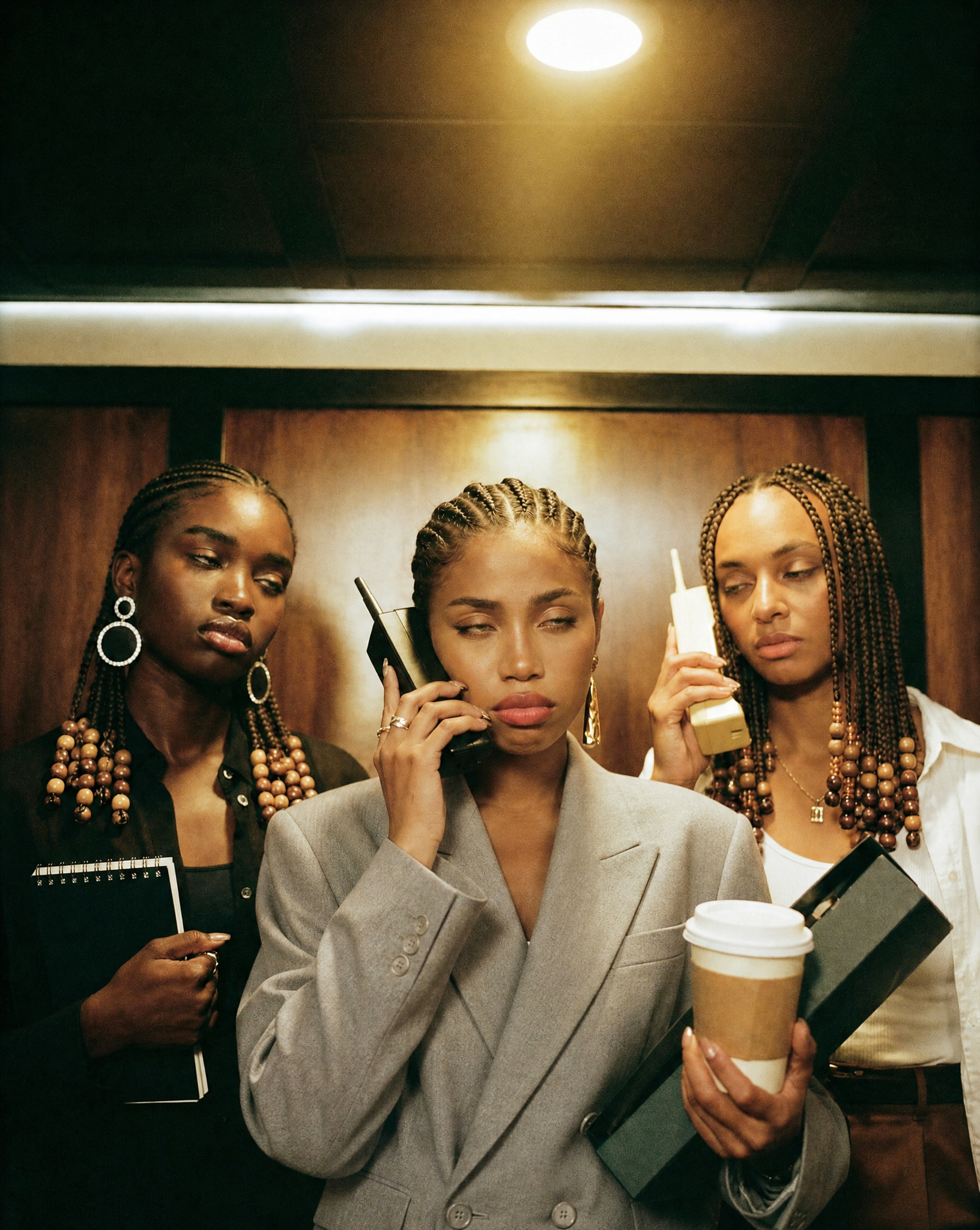 Three professionals in an elevator holding phones, coffee, and work folders.