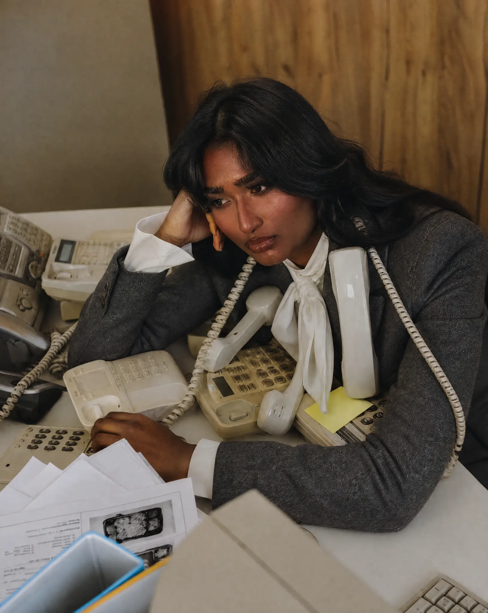 Professional at a desk surrounded by office phones and paperwork.